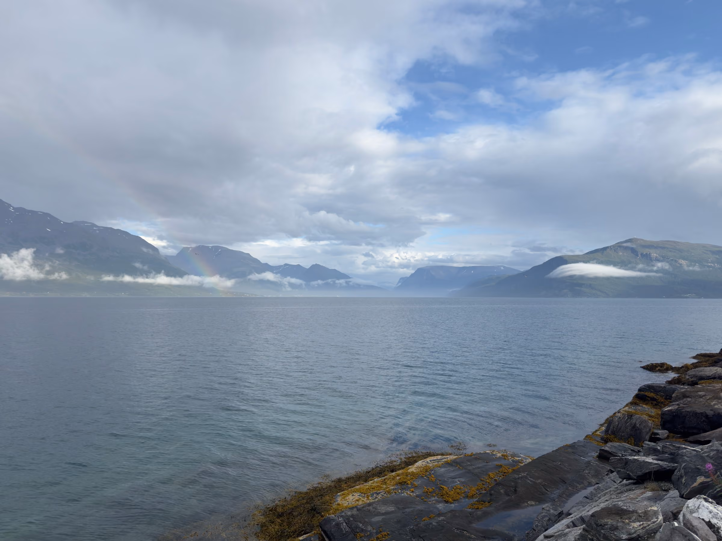 Blasser Regenbogen über der Bergflanke am Lyngenfjord, Wolken hängen tief im Tal